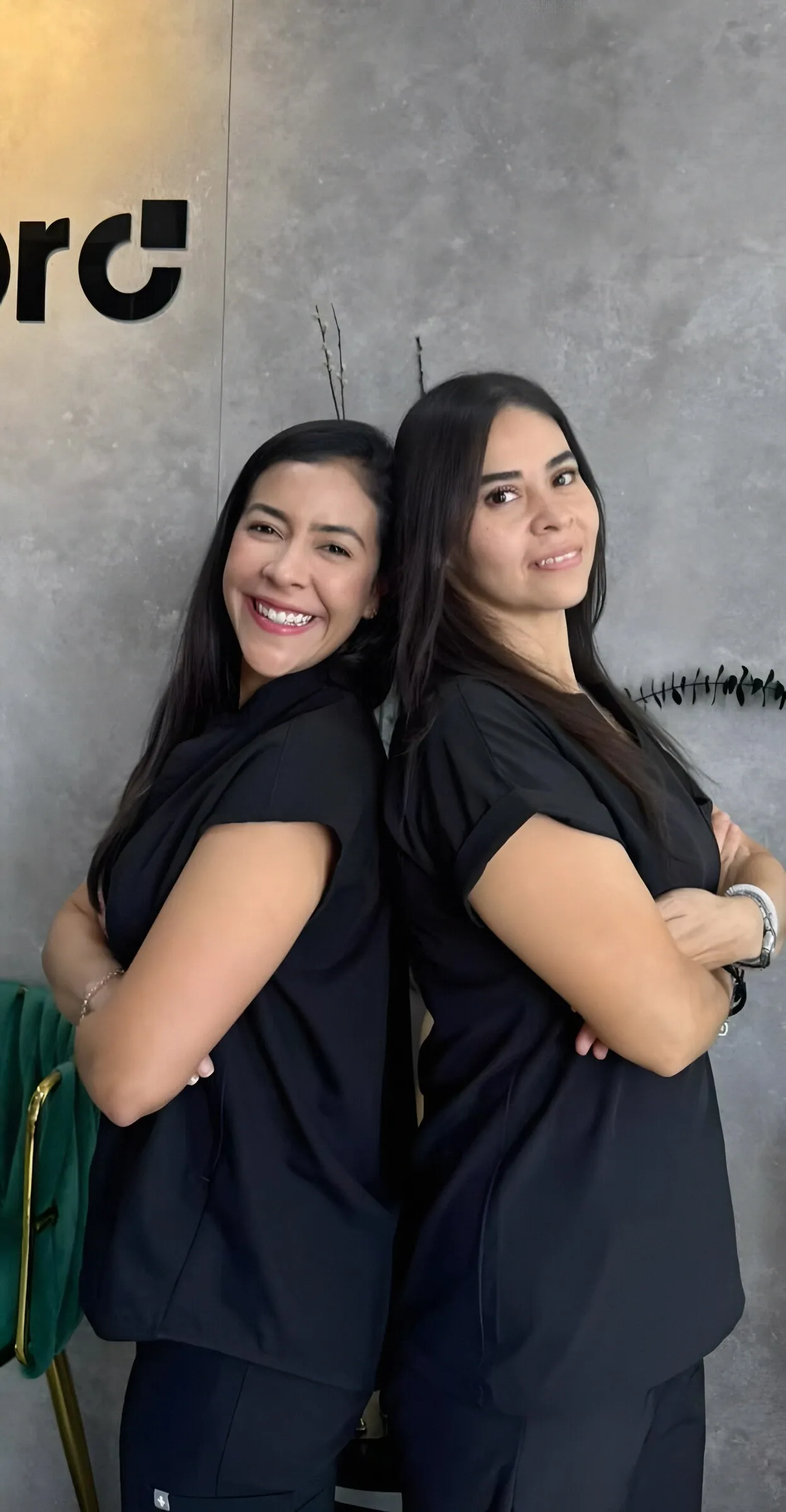 Dos odontólogas de Wepro con uniforme negro frente al muro de concreto con el logo de la clínica