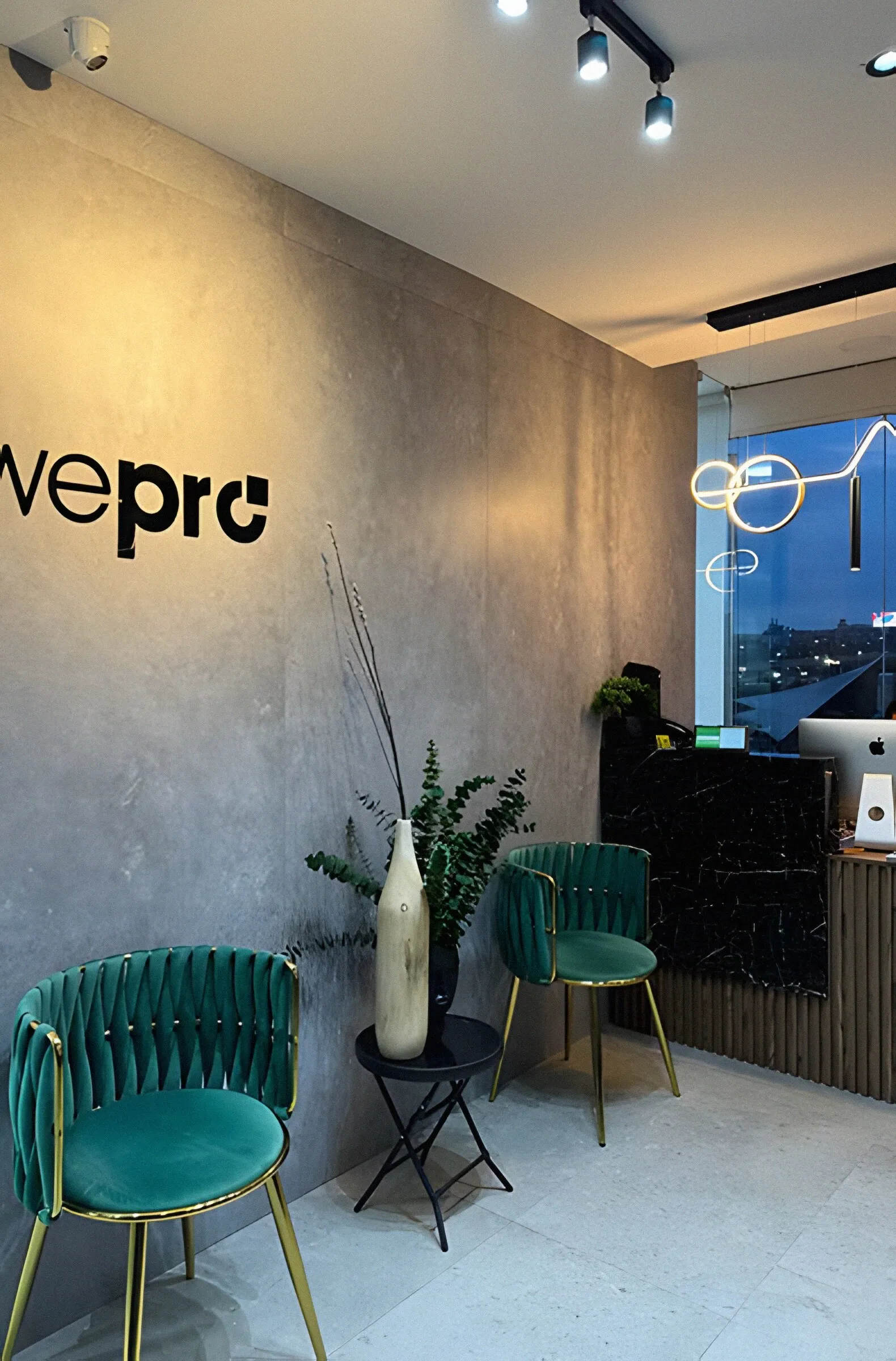 Recepción de Wepro con muro de concreto, el logo de la clínica y sillas de terciopelo verde